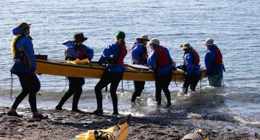a group of students carry a kayak into the water on an outward bound expedition in the pacific northwest